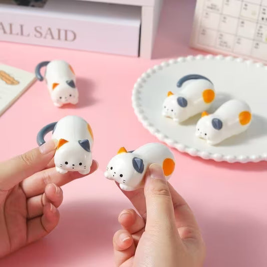 Small white animal figurines with orange and gray accents held by a hand on a pink background.