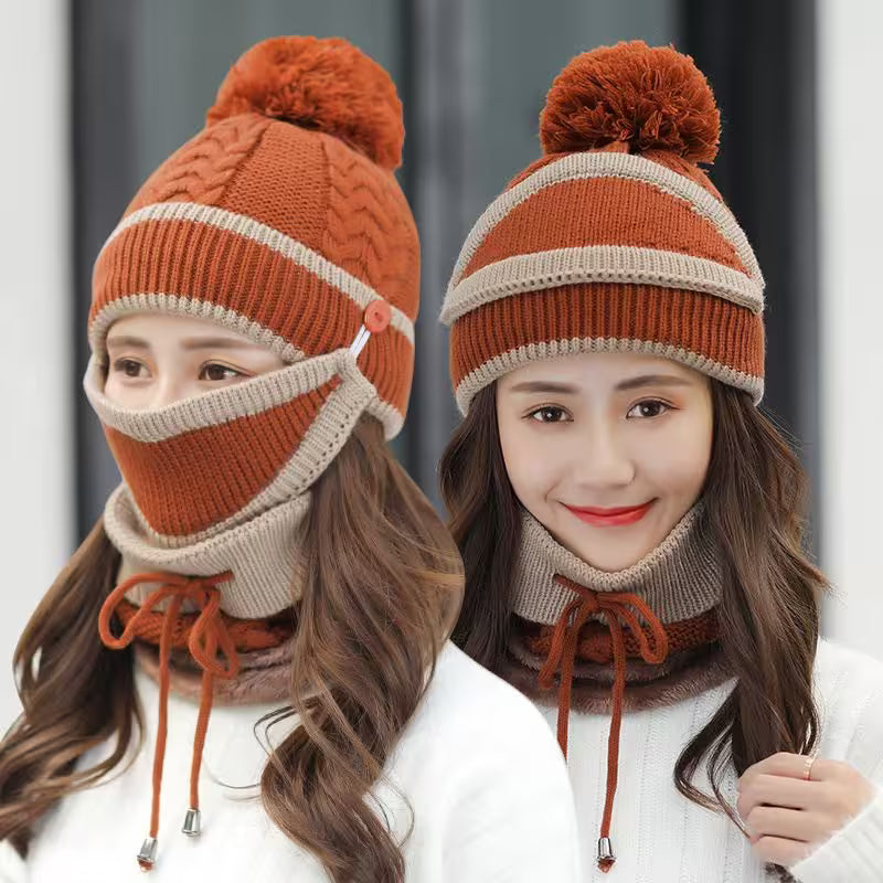 Two women wearing matching orange and beige knitted hats with pom-poms and scarves against a neutral background.