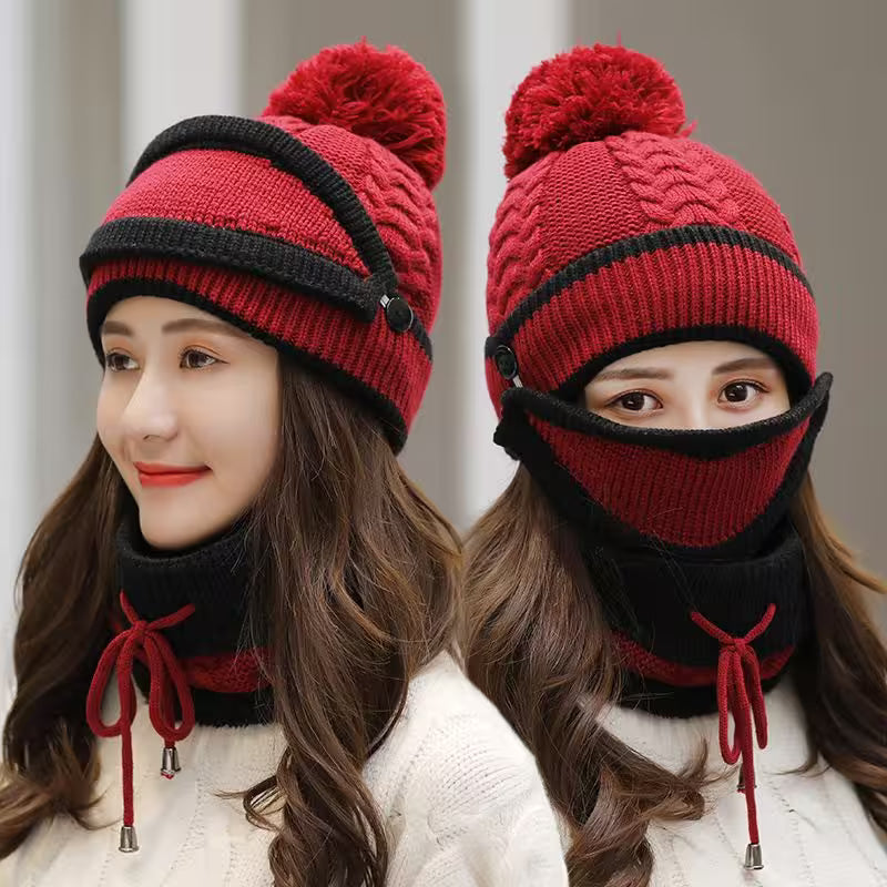 Red and black knitted hat with pom-pom and face mask worn by a model against a neutral background
