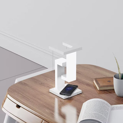 Modern desk setup with a white lamp, smartphone, and open book on a wooden surface.