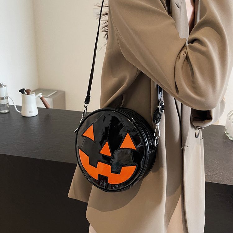 Person holding a black round bag with orange jack-o'-lantern design, wearing a beige coat.