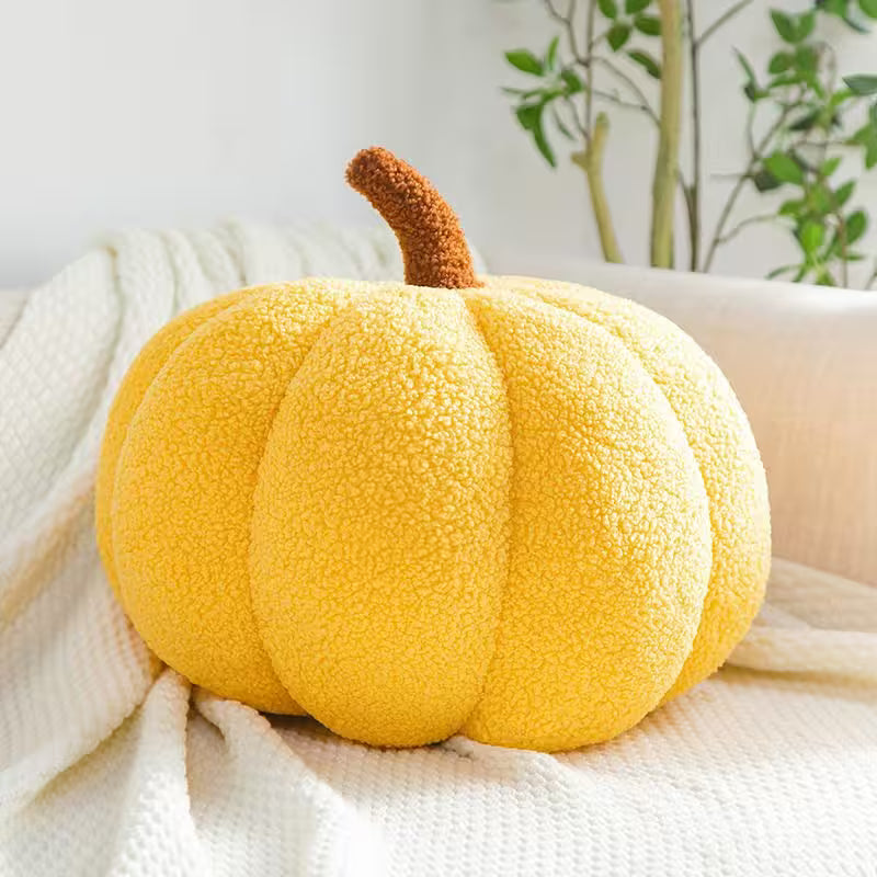 Yellow plush pumpkin on a white blanket with a plant in the background